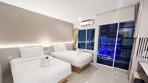 Una habitación de hotel con dos camas, un ventanal con vistas a la ciudad y un balcón con barandilla.