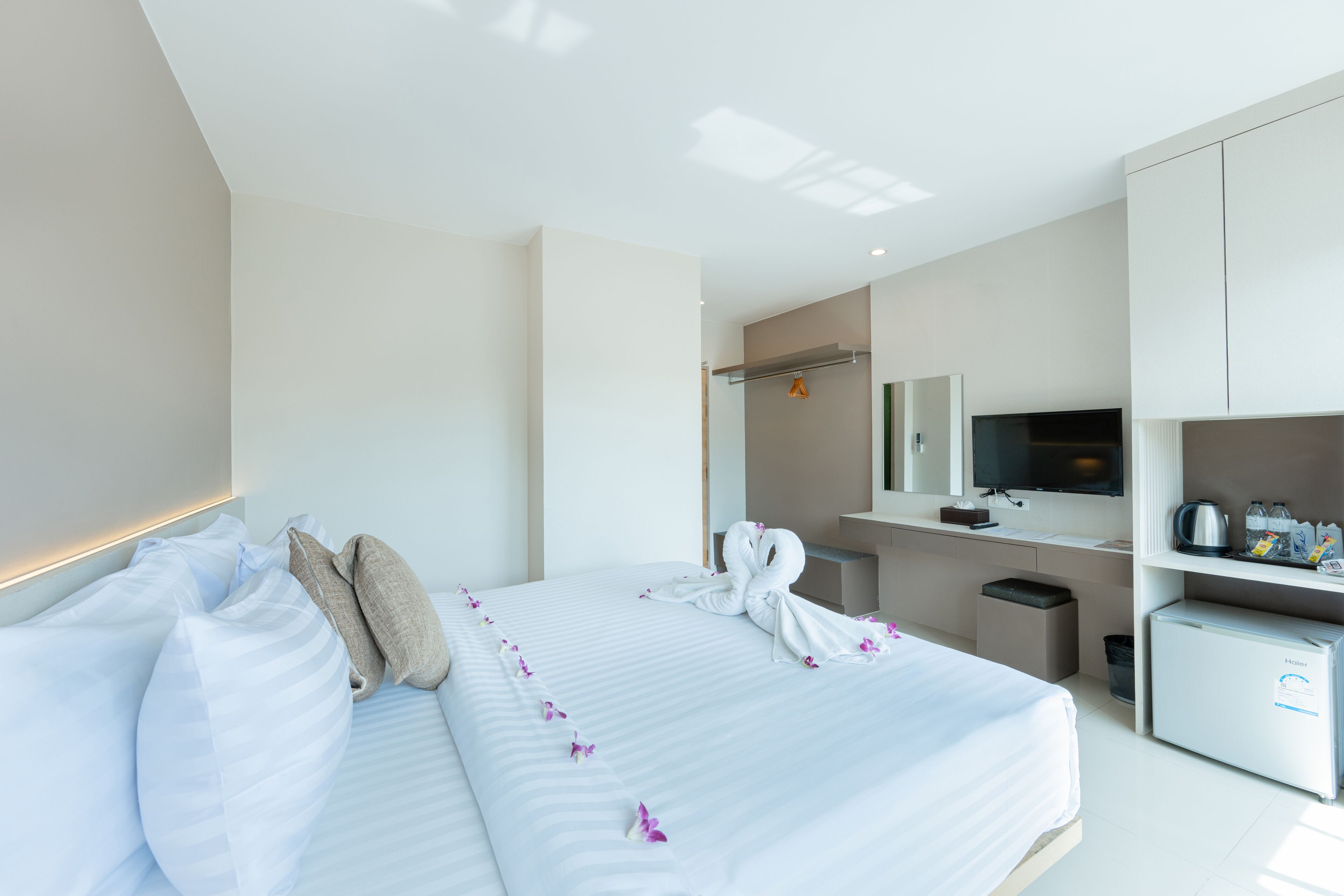A modern hotel room with a large bed, a desk with a flat-screen TV, a mini-fridge, and a small trash bin.