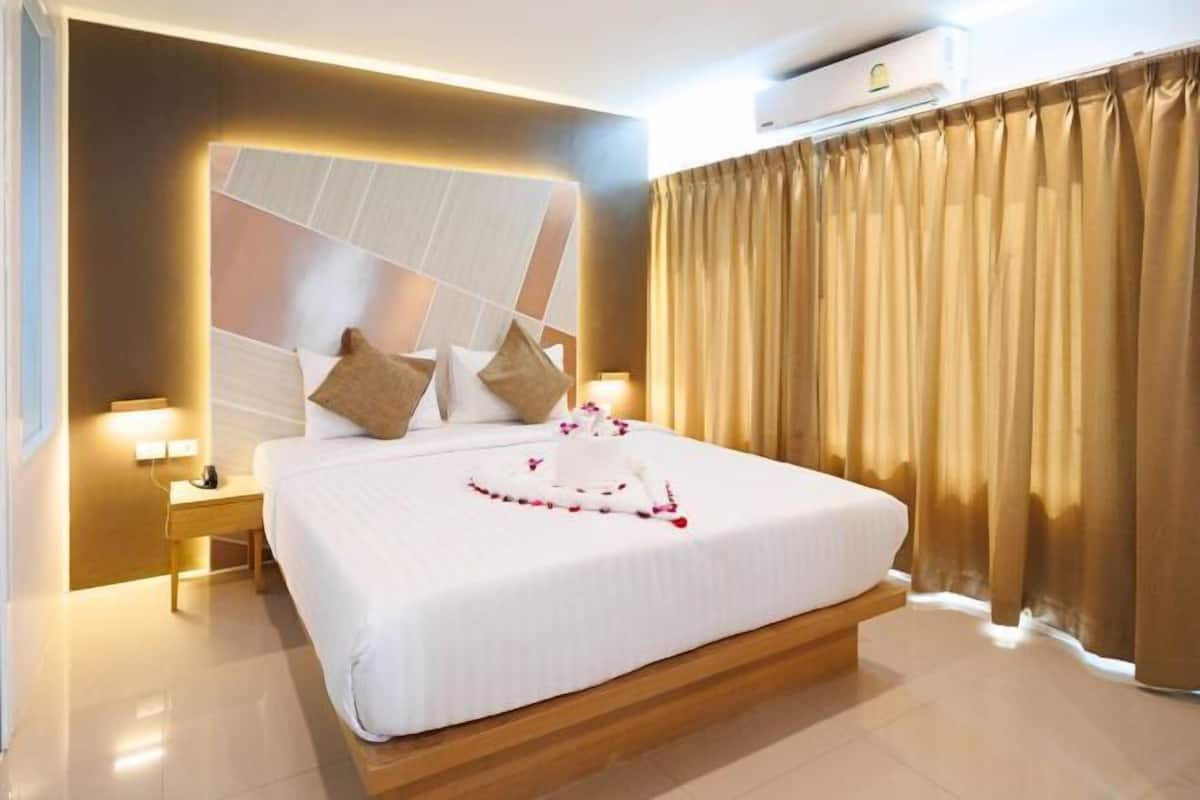 Een hotelkamer met een groot bed, een nachtkastje, een wandairco en een raam met gordijnen.