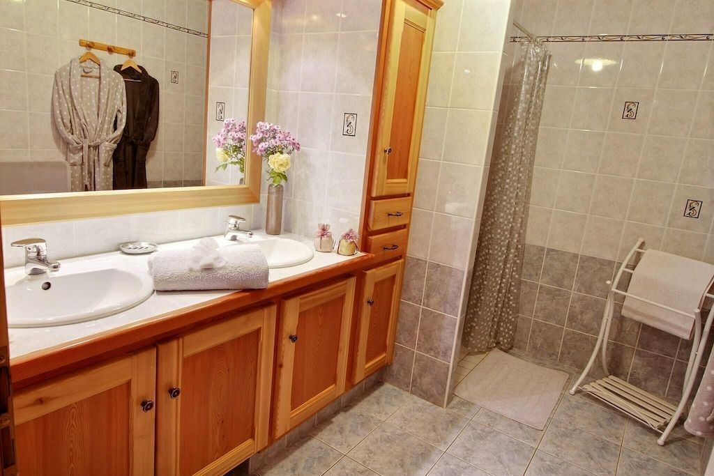 A bathroom with two sinks, a mirror, wooden cabinets, a shower area, and a towel rack.