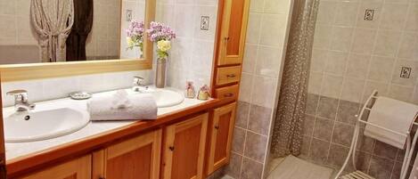 A bathroom with two sinks, a mirror, wooden cabinets, a shower area, and a towel rack.