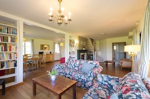 A spacious living area with a floral sofa, wooden coffee table, and a chandelier.