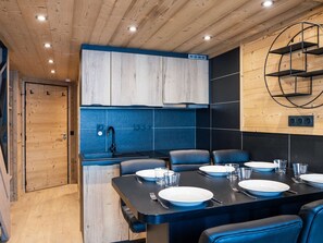 Cozinha moderna com armários de madeira, painel de parede azul e um espaço de jantar com mesa preta e cadeiras azuis.
