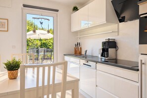 A modern kitchen with white cabinetry, a coffee maker, and a dining area with a table and chairs.