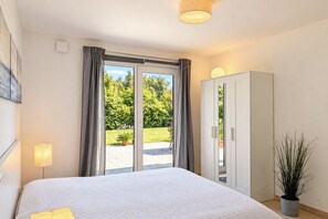 A hotel room with a bed, a wardrobe, a potted plant, and a view of a garden through a sliding door.