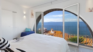 A bedroom with a large bed, a view of the sea, and a balcony with a railing.