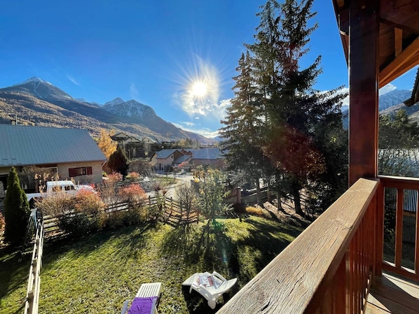 Un balcón con vistas a un paisaje montañoso, una terraza de madera y una zona verde con una silla y una mesa.