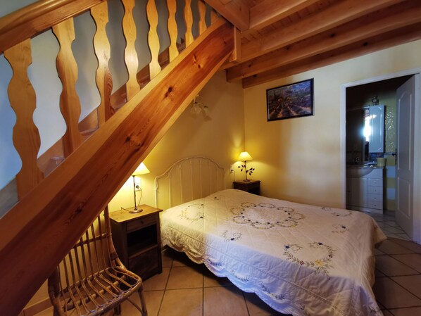 Une chambre avec un escalier en bois, un lit recouvert d’une couvre-lit à motifs floraux, deux lampes de chevet et un tableau accroché au mur.