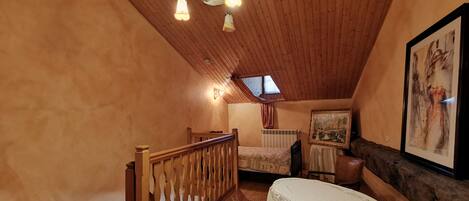 Ein gemütliches Schlafzimmer im Dachgeschoss mit Holzbalkendecke, einem Bett mit gemustertem Überwurf, einem kleinen Tisch mit Spitze und einem Bild an der Wand.