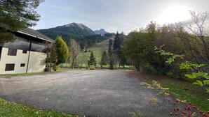 Una strada privata lastricata conduce a un edificio con tetto spiovente, circondato da alberi e con montagne sullo sfondo.