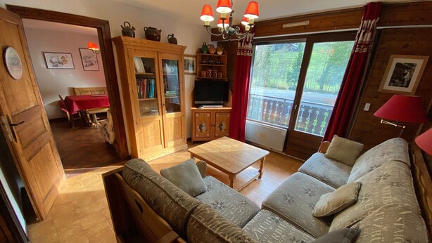 Un accogliente soggiorno con divano, mobiletto in legno, televisore e un balcone con vista.