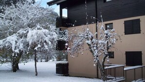 Un edificio con facciata beige e tetto scuro, circondato da alberi innevati e una recinzione metallica.