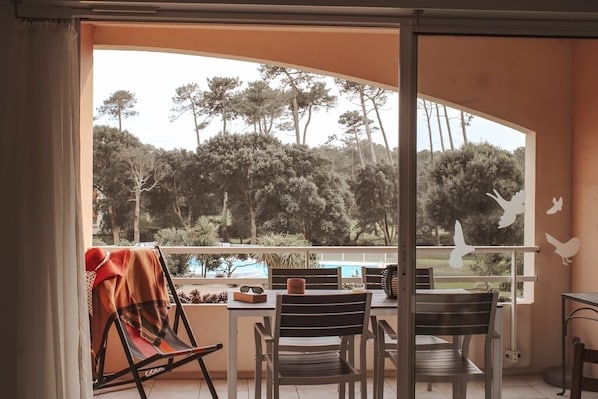 A balcony with a table and chairs, overlooking a pool and trees.