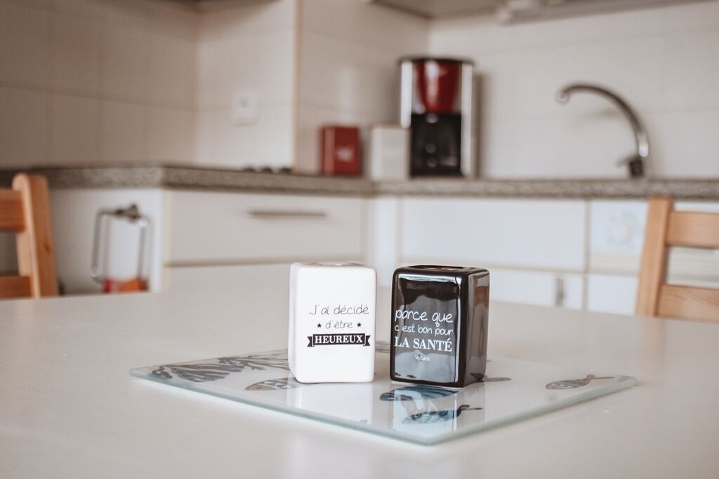 Une cuisine avec une machine à café, un récipient blanc et un récipient noir sur une table en verre.