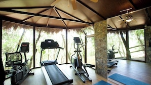 Une salle de sport équipée de tapis de course, de vélos elliptiques et de tapis de sol, avec de grandes fenêtres et un plafond en bois.