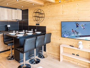 Cozinha moderna com área de jantar, parede de madeira com design geométrico e uma TV exibindo um evento de esqui.