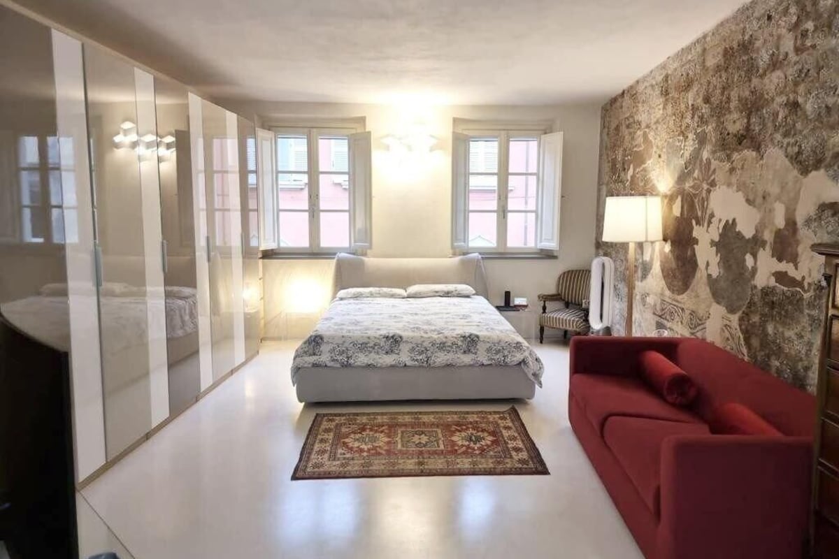 A bedroom with a bed, a red sofa, a patterned rug, and a wall with a textured design.