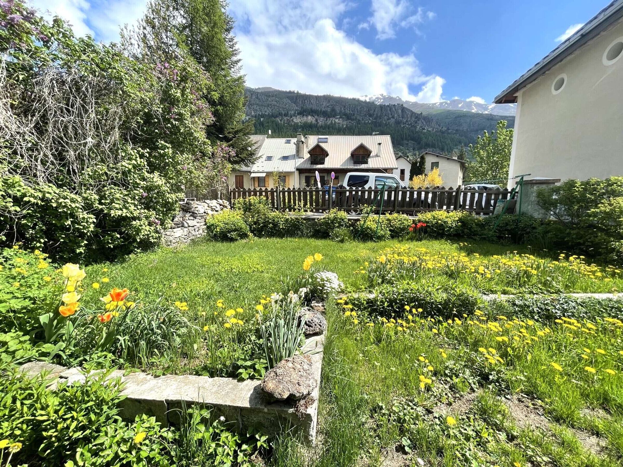 A garden with a stone wall, yellow flowers, and a wooden fence.