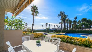 An outdoor patio with a round table and chairs, a pool, and palm trees. - Ground floor first sealine 009 UHC Los Flamencos (Miami Playa)
