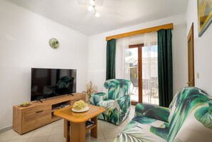 A living room with a flat-screen TV, wooden furniture, a plant, and a view of the outdoors through a window with curtains. - House Maria (Istria - Bokordići) (Bokordići)