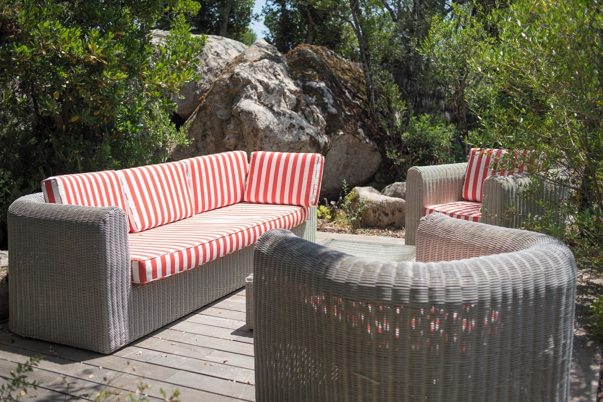 A wicker outdoor seating area with striped cushions, set against a backdrop of rocks and greenery.
