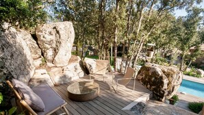 Une terrasse en bois avec un fauteuil de relaxation et un repose-pieds, entourée de gros rochers et d’arbres.