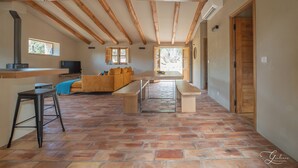 Un vaste espace de vie doté d’un plafond haut, de poutres apparentes, d’un sol carrelé en pierre, d’un canapé, d’une table et d’un banc.