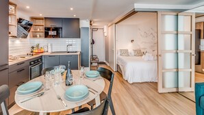 Eine moderne Küche mit Essbereich für vier Personen, ein Bett mit Blick und eine Schiebetür zum Schlafzimmer.