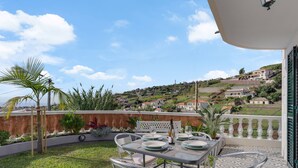 A terrace with a table set for dining, overlooking a hilly landscape with houses. - Melody House of Ponta do Sol (Ponta do Sol)