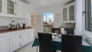 A dining area with a table set for two, white cabinets, and a view through a door to the outside. - Melody House of Ponta do Sol (Ponta do Sol)