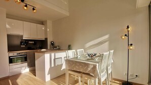 A modern kitchen with white cabinets, a built-in oven, and a dining area with a table and chairs. - Carnac: 3-room Duplex, 4 pers, Close to beach, Wifi (Carnac)