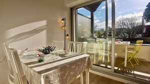 A dining area with a table set for two, white chairs, and a glass partition. - Carnac: 3-room Duplex, 4 pers, Close to beach, Wifi (Carnac)