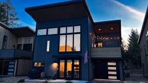 A modern two-story house with large windows, a flag, and a well-lit entrance.