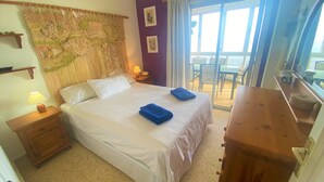 A hotel room with a bed, a wooden nightstand, a lamp, a large woven tapestry, a sliding glass door to a balcony, and a wooden dresser. - Salinetas, first line of the sea and beach for 4 people (telde)