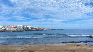 A coastal town with buildings along the shore, a sandy beach, and the ocean. - Salinetas, first line of the sea and beach for 4 people (telde)