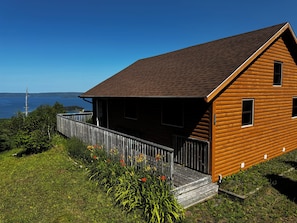 Une cabane en bois dotée d’un porche, entourée de verdure et offrant une vue sur une étendue d’eau.