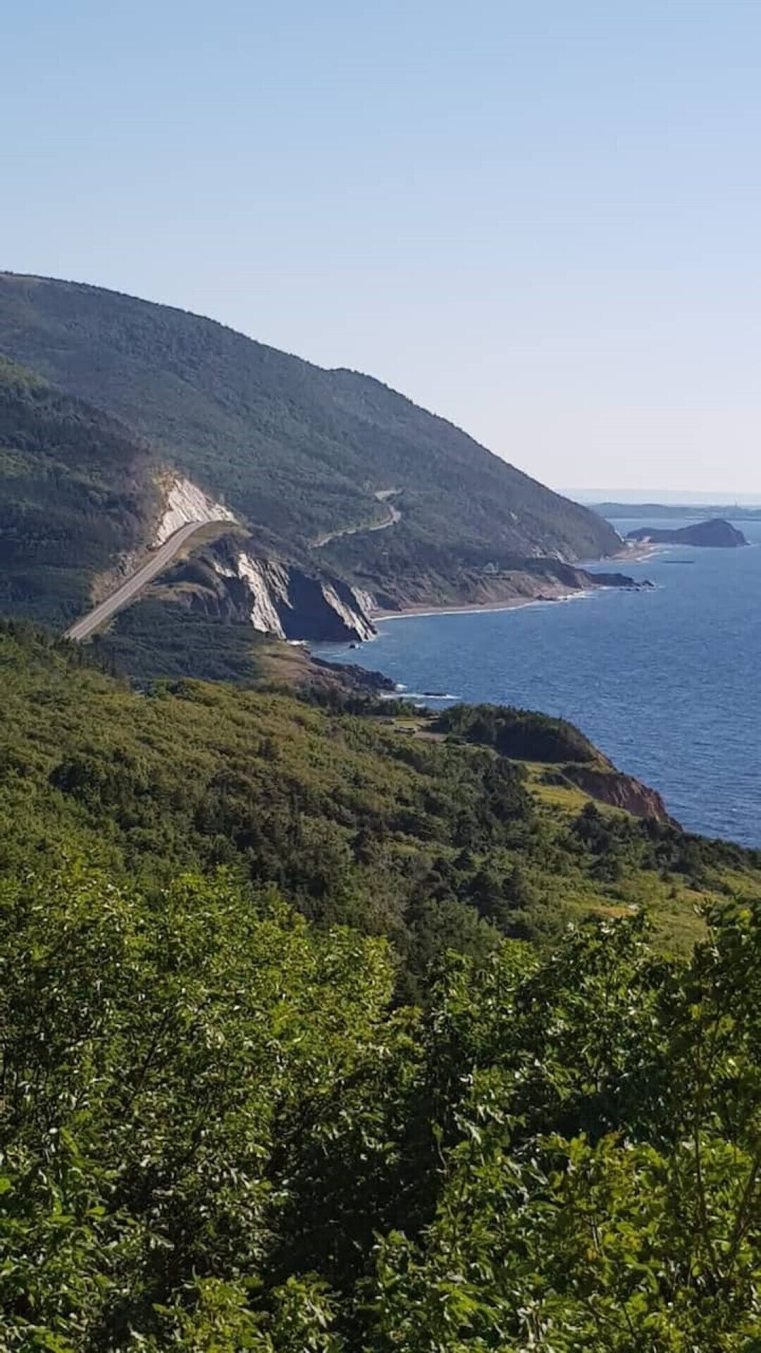Eine Küstenstraße schlängelt sich durch eine gebirgige Landschaft mit üppiger Vegetation und Blick auf den Ozean.