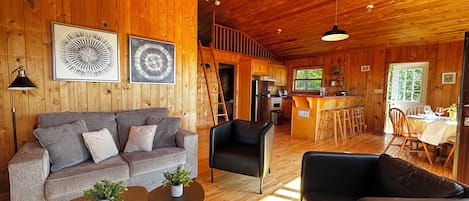 L’intérieur d’un chalet en bois comprend un canapé, des fauteuils, un coin repas et une cuisine.