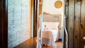 Un dormitorio con cabecera de madera, un colgador redondo tejido en la pared y una cama con ropa blanca y una pequeña planta.