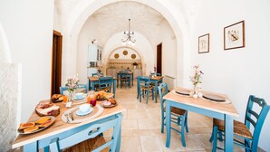 Un área de comedor con sillas y mesas azules, una cocina al fondo y un techo abovedado blanco.