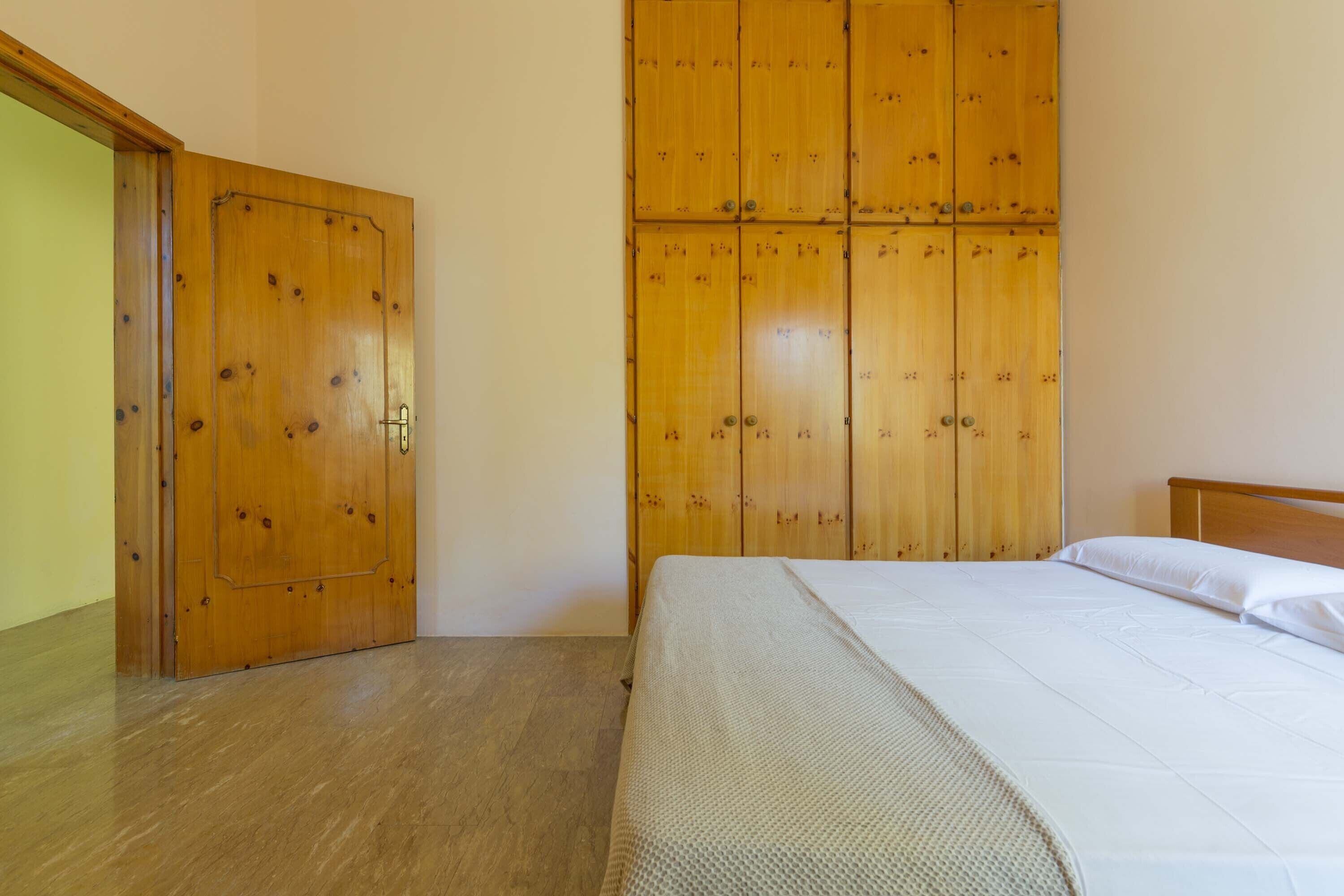Un dormitorio con un armario de madera, una cama con ropa de cama blanca y piso de madera.