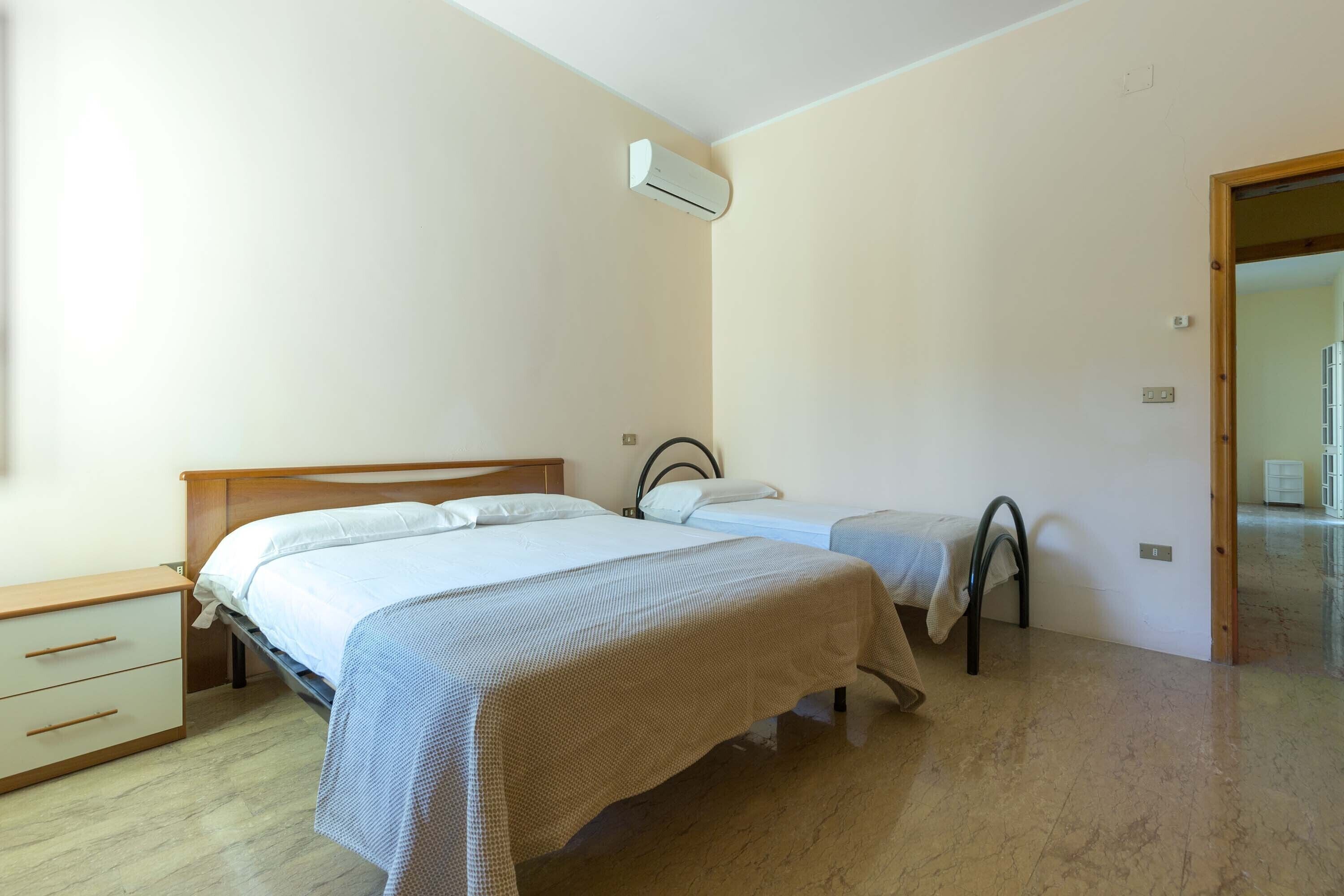 A bedroom with two beds, a wooden nightstand, a small table, and a door leading to another room.