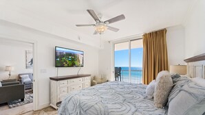 Een slaapkamer met een groot bed, een plafondventilator, een televisie en uitzicht op de oceaan door een schuifdeur.
