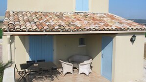 Un edificio con techo de tejas, una mesa con sillas y un pequeño espacio para sentarse.
