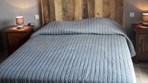 Un dormitorio con cabecera de madera, colcha estampada, dos lámparas de noche y un interruptor de luz en la pared.