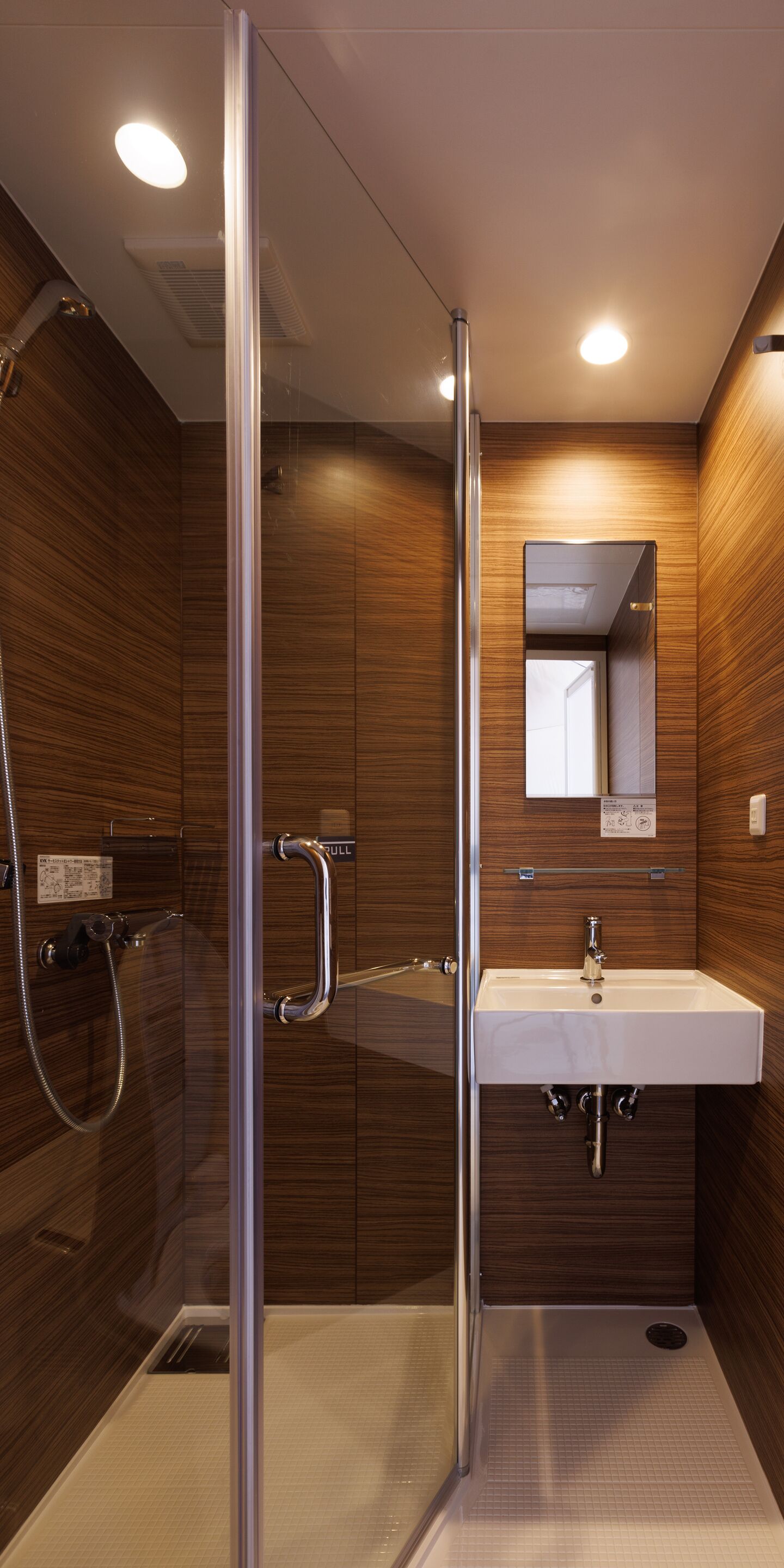 A modern bathroom with a glass shower enclosure, a sink with a mirror above it, and wooden paneling on the walls.