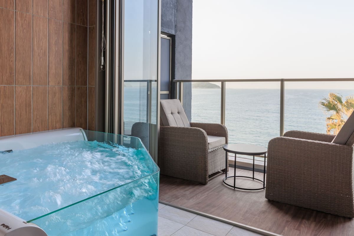 A modern bathroom with a glass-enclosed jacuzzi, wooden paneling, and a view of the sea.