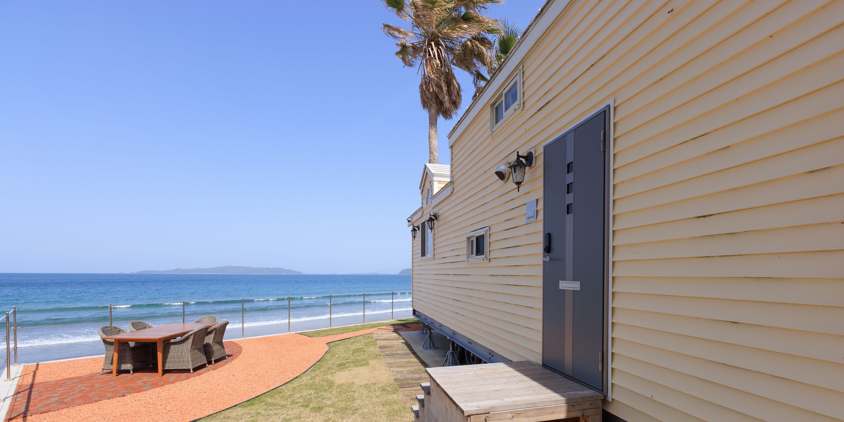 A beachside property with a patio, a table, and chairs, overlooking the ocean.