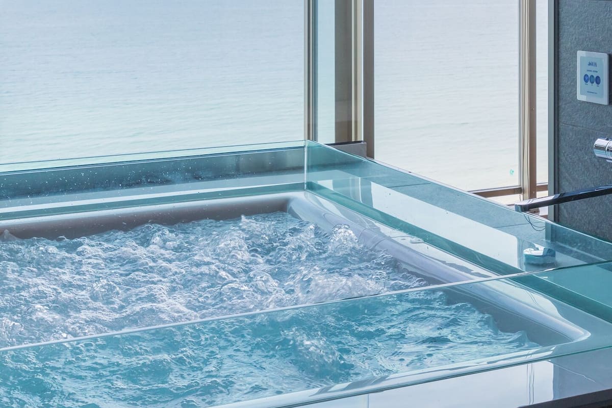 A glass-enclosed hot tub with a view of the sea.