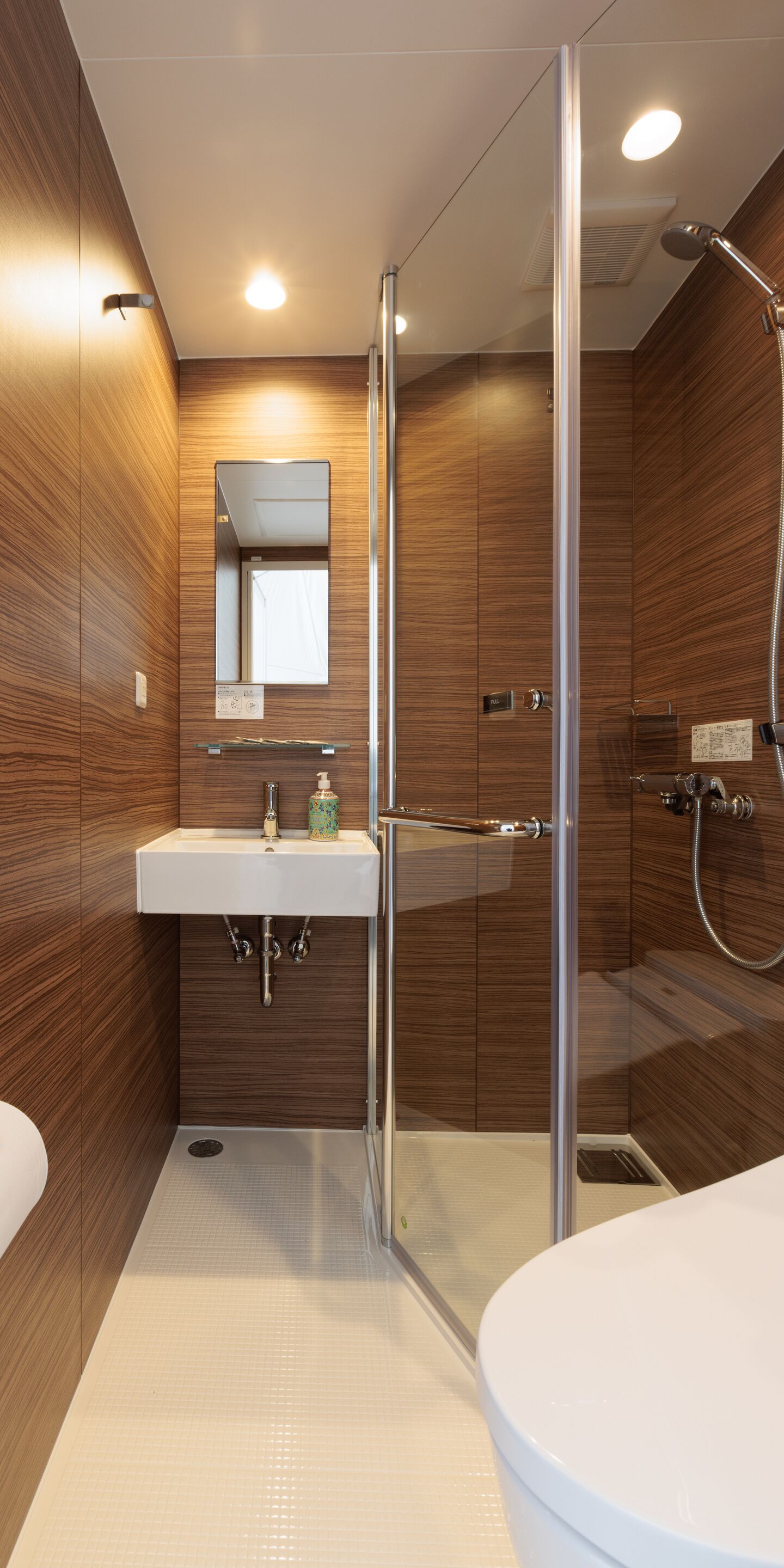 Een moderne badkamer met een glazen douchecabine, een wit wastafelmeubel met spiegel en houten lambrisering.